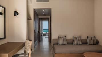 Una habitación de hotel moderna con un escritorio de madera, una silla acolchada, un sofá con almohadones a rayas y vistas al océano a través de un vano abierto.