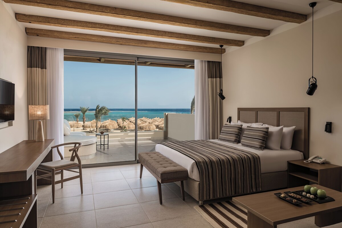 Een moderne hotelkamer met een groot bed, een bureau en uitzicht op het strand.