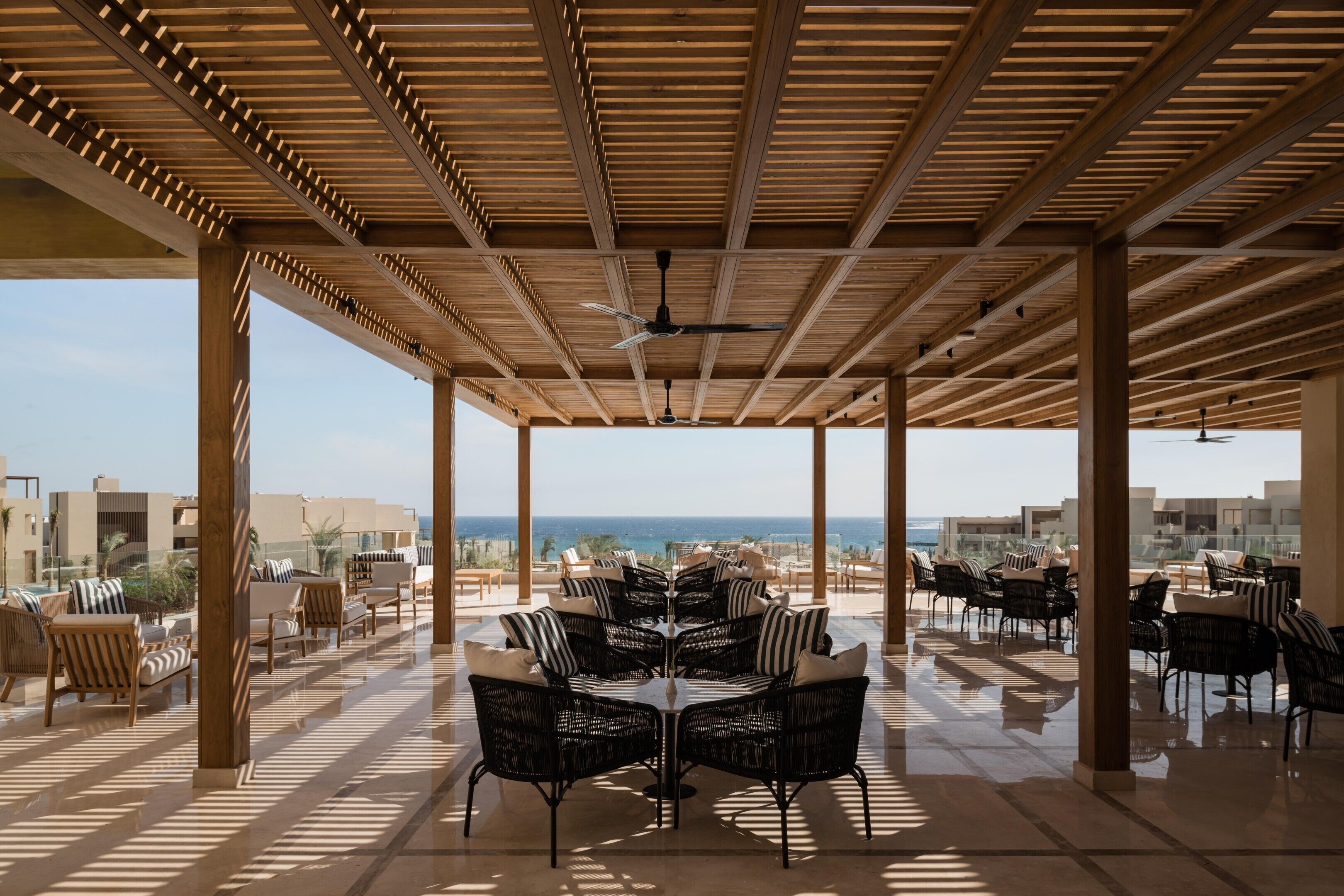 An outdoor patio with a view of the sea, furnished with wicker chairs and tables.