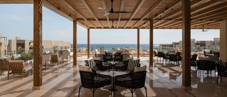 An outdoor patio with a view of the sea, furnished with wicker chairs and tables.