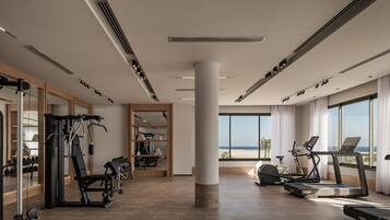 Un gimnasio moderno con equipo de ejercicio, ventanas amplias y vista a la playa.