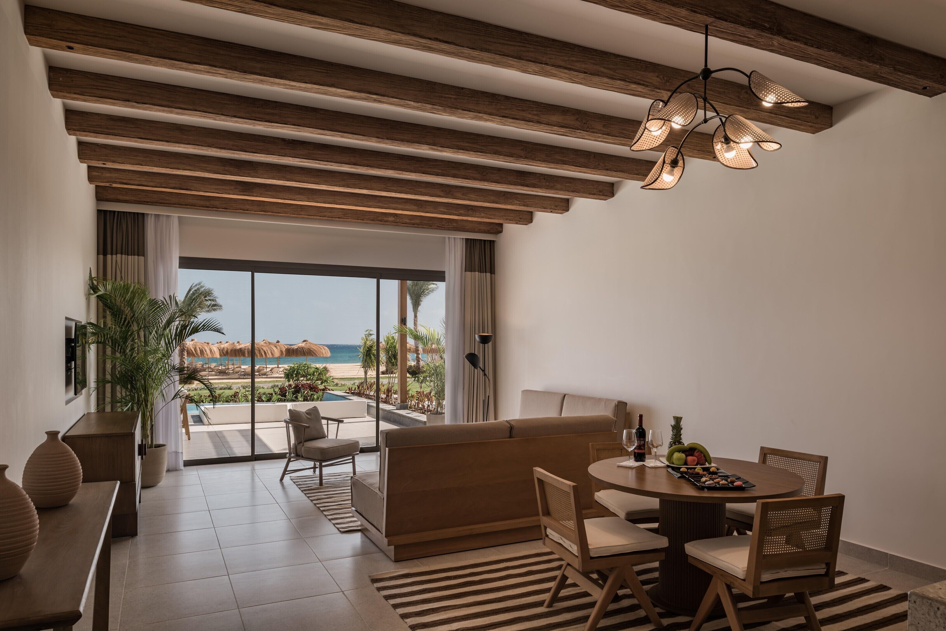 A modern hotel room with a balcony, a dining area, and a view of the beach.