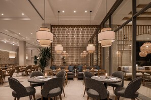 A modern dining area with round tables, grey upholstered chairs, and hanging pendant lights.