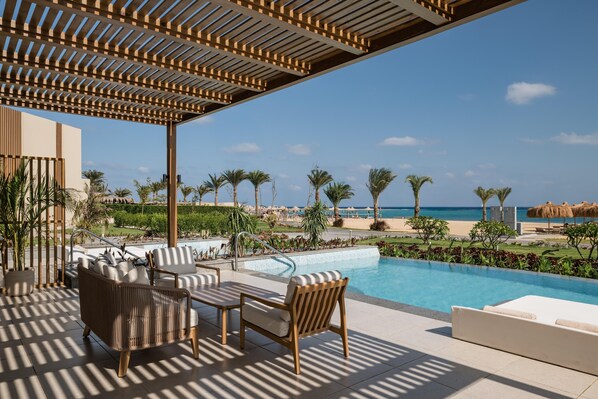A poolside area with lounge chairs and a pergola, overlooking a beach and ocean. - JAZ Elite Riviera (Marsa Alam)