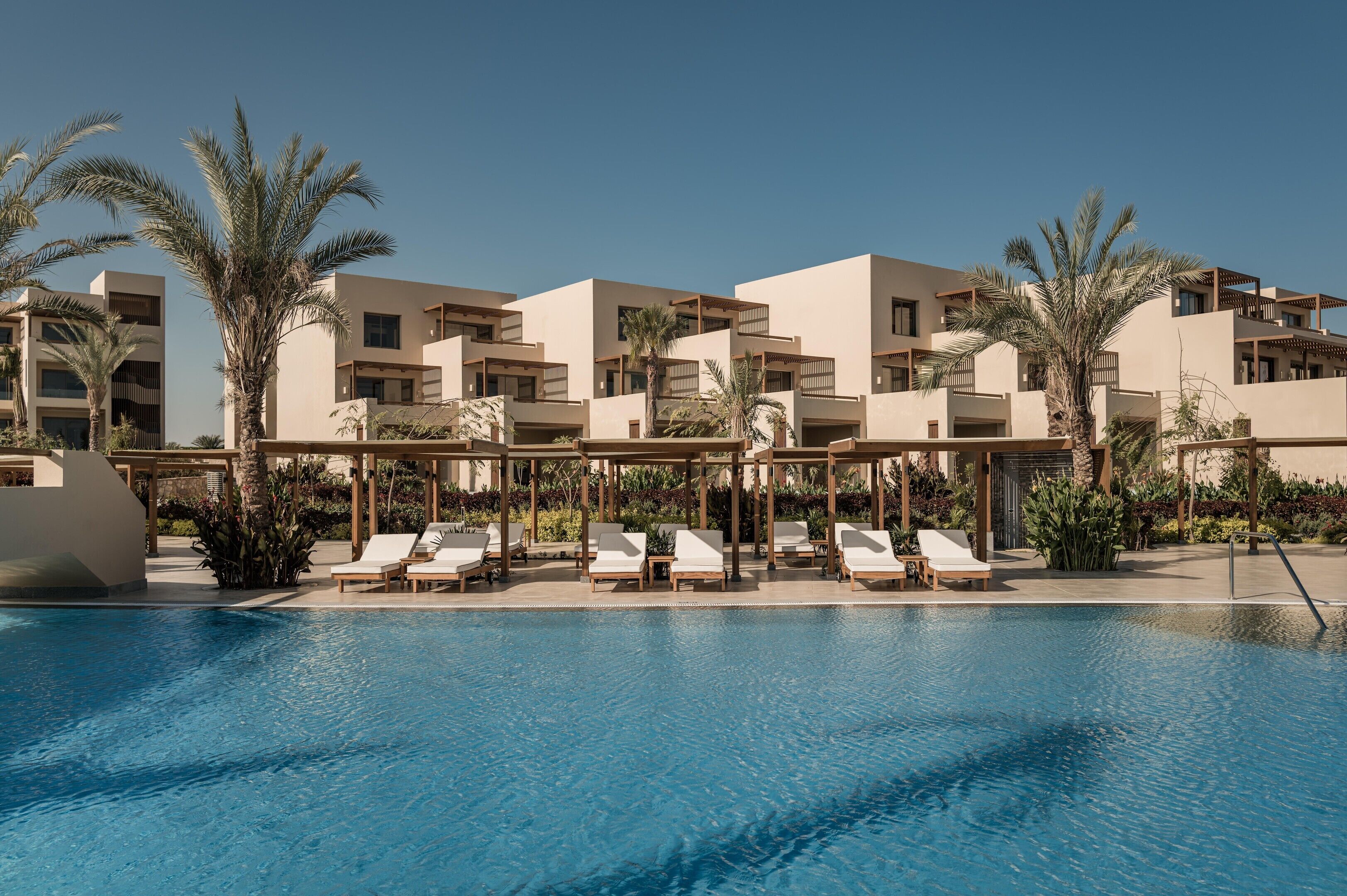 A modern hotel with a pool area, multiple balconies, and palm trees.
