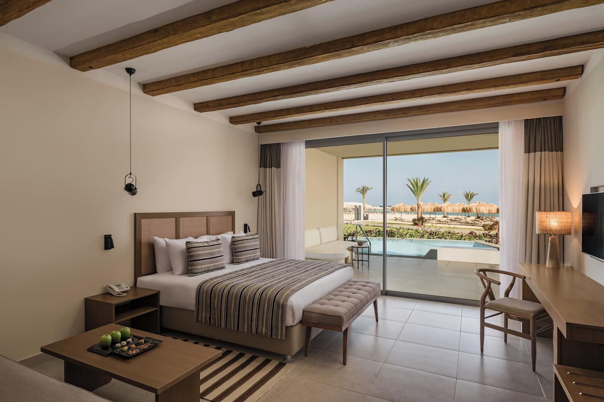 A modern hotel room with a large bed, a desk, and a view of a pool and palm trees.