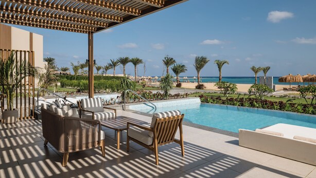 A poolside area with lounge chairs and a pergola, overlooking a beach and ocean. - JAZ Elite Riviera (Marsa Alam)