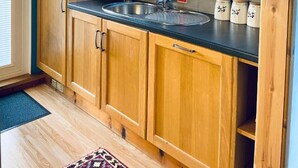 Cocina compacta con armarios de madera, pileta de acero inoxidable y ventana con persianas.