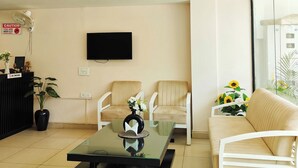 A reception area with a black reception desk, two beige armchairs, a glass coffee table, and a beige sofa. - La Cozy Residency (Gurugram)