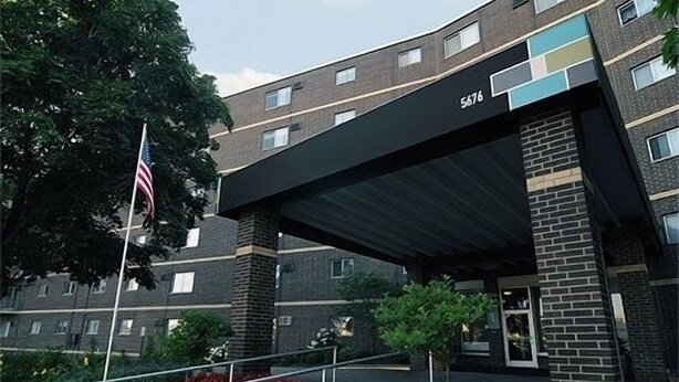 Un edificio de varios pisos con fachada de ladrillo, un toldo negro sobre la entrada y una bandera estadounidense.