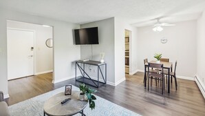 Ein modernes Wohnzimmer mit Flachbildfernseher, einem Esstisch mit Stühlen, einem Couchtisch und einer kleinen Pflanze.