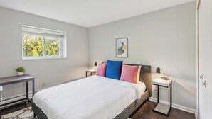 Ein modernes Schlafzimmer mit Bett, Nachttischen, einem Fenster und einer kleinen Pflanze.