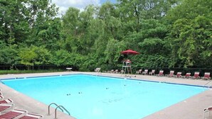 Una piscina rectangular con una escalera, rodeada de sillas de descanso y una sombrilla, todo en color rojo.