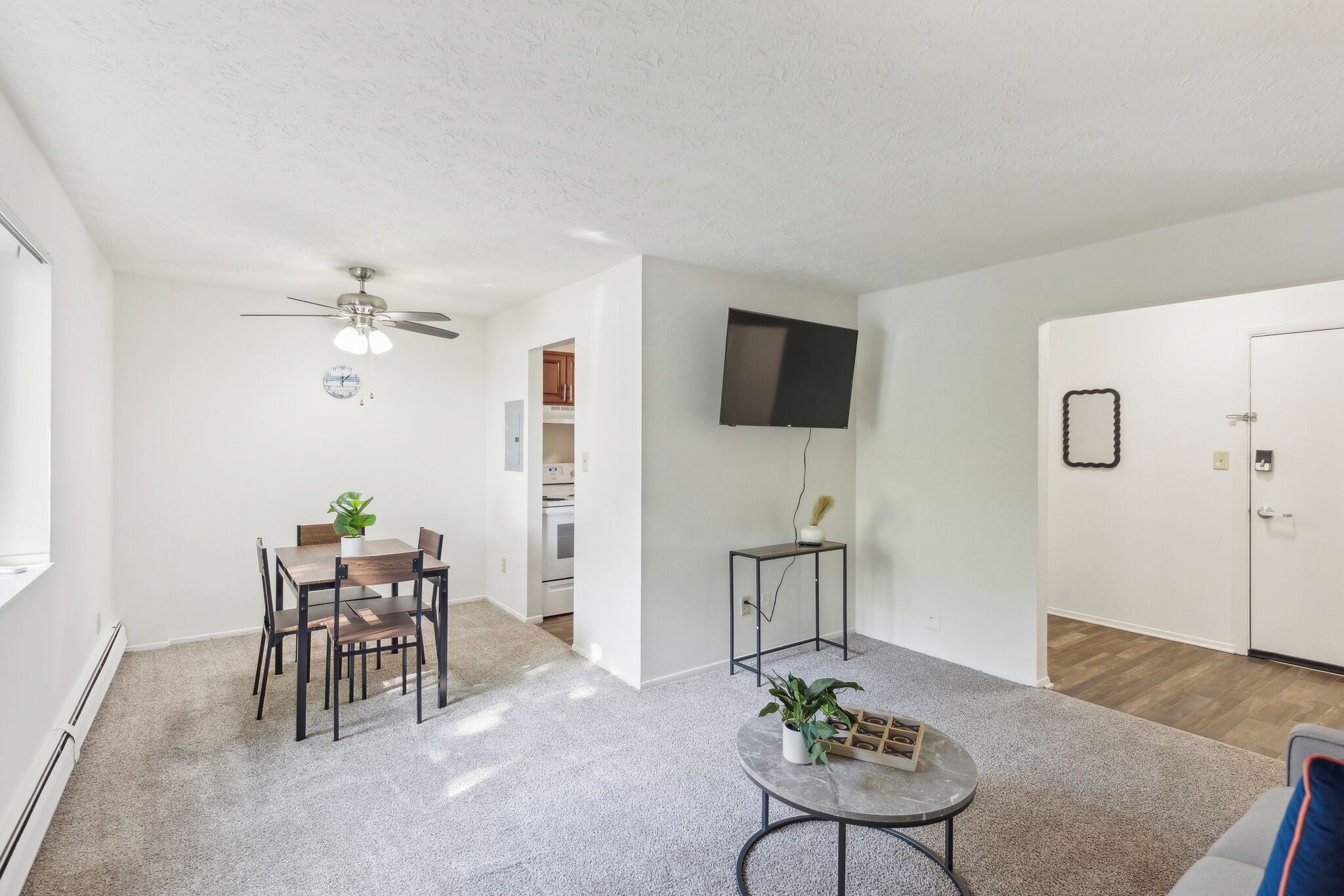 A modern living room with a dining area, a ceiling fan, a flat-screen TV, and a door with a mirror.