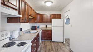 Une cuisine de taille réduite, dotée de meubles en bois, d’une cuisinière blanche, d’un four à micro-ondes et d’un réfrigérateur.