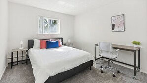 Ein Schlafzimmer mit Bett, Schreibtisch, Stuhl, Fenster und einem Wandbild.