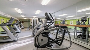 A gym with multiple treadmills and exercise equipment, a mirrored wall, and green walls.