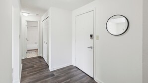 Un pasillo con paredes blancas, piso de madera y una puerta con un espejo redondo.