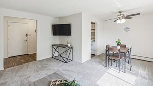 Un salon moderne comprenant un coin repas, un ventilateur de plafond, un téléviseur à écran plat et une petite plante posée sur une table d’appoint.