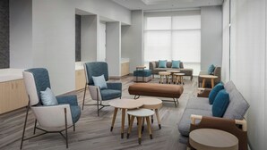 Zona lounge moderna con diverse disposizioni di posti a sedere, tra cui divani e poltrone, e piccoli tavolini rotondi.