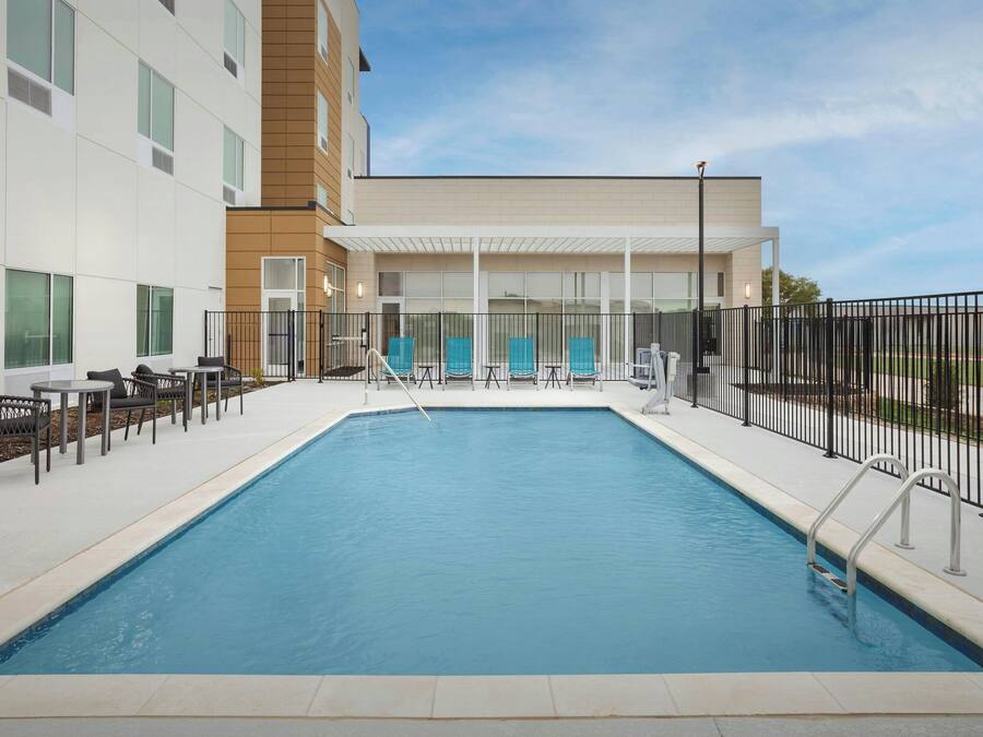 A swimming pool with lounge chairs and a covered seating area, surrounded by a fence.