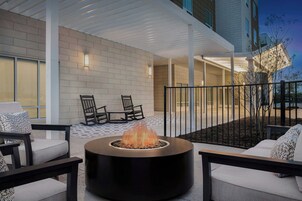 An outdoor seating area with a circular fire feature, chairs, and a white brick wall.