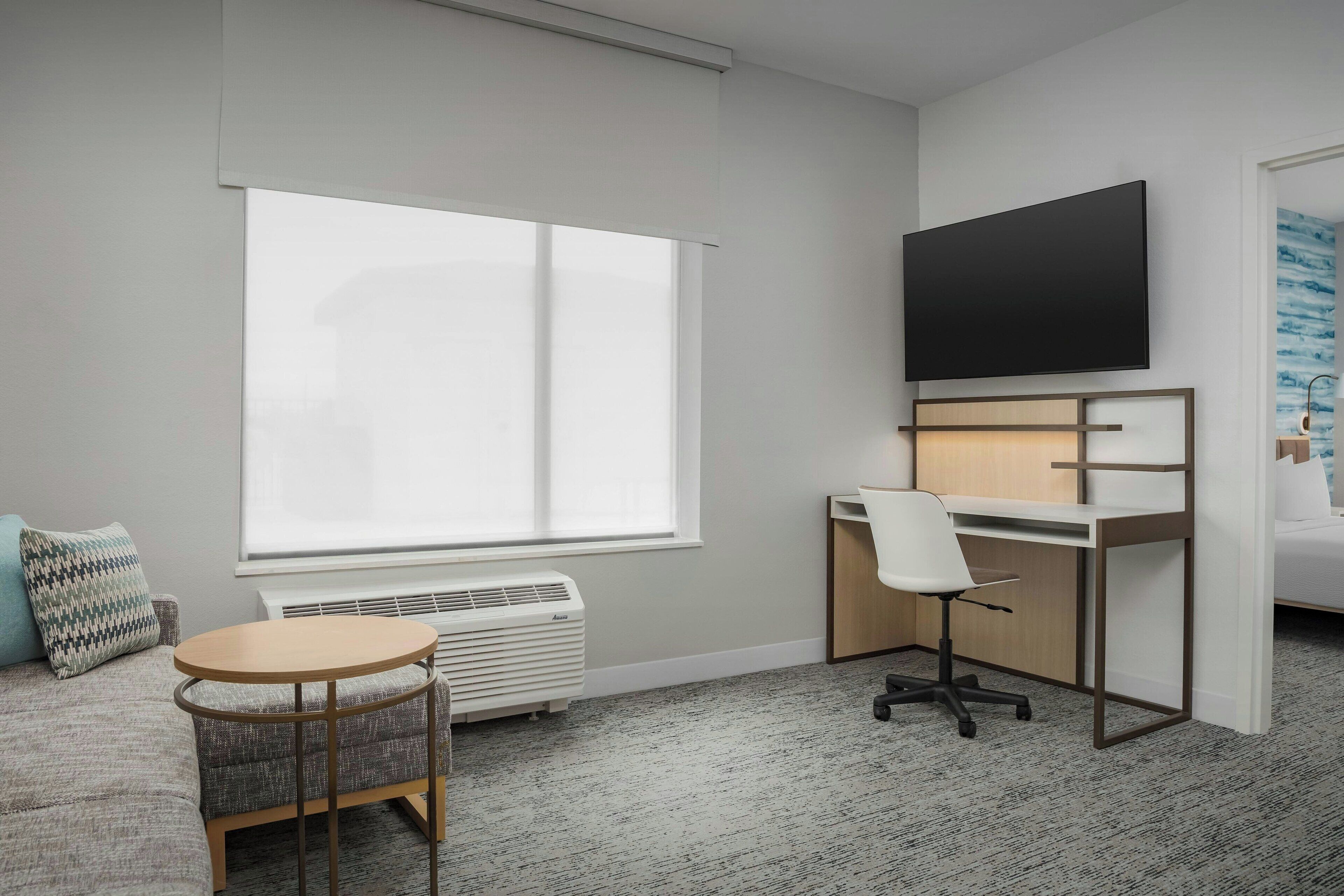 Une chambre d’hôtel moderne dotée d’une grande fenêtre, d’un bureau avec une chaise, d’un téléviseur à écran plat et d’un lit.