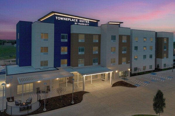 Un hôtel à plusieurs étages, avec une enseigne indiquant « Towneplace Suites by Marriott », et un espace extérieur couvert avec des tables et des chaises.
