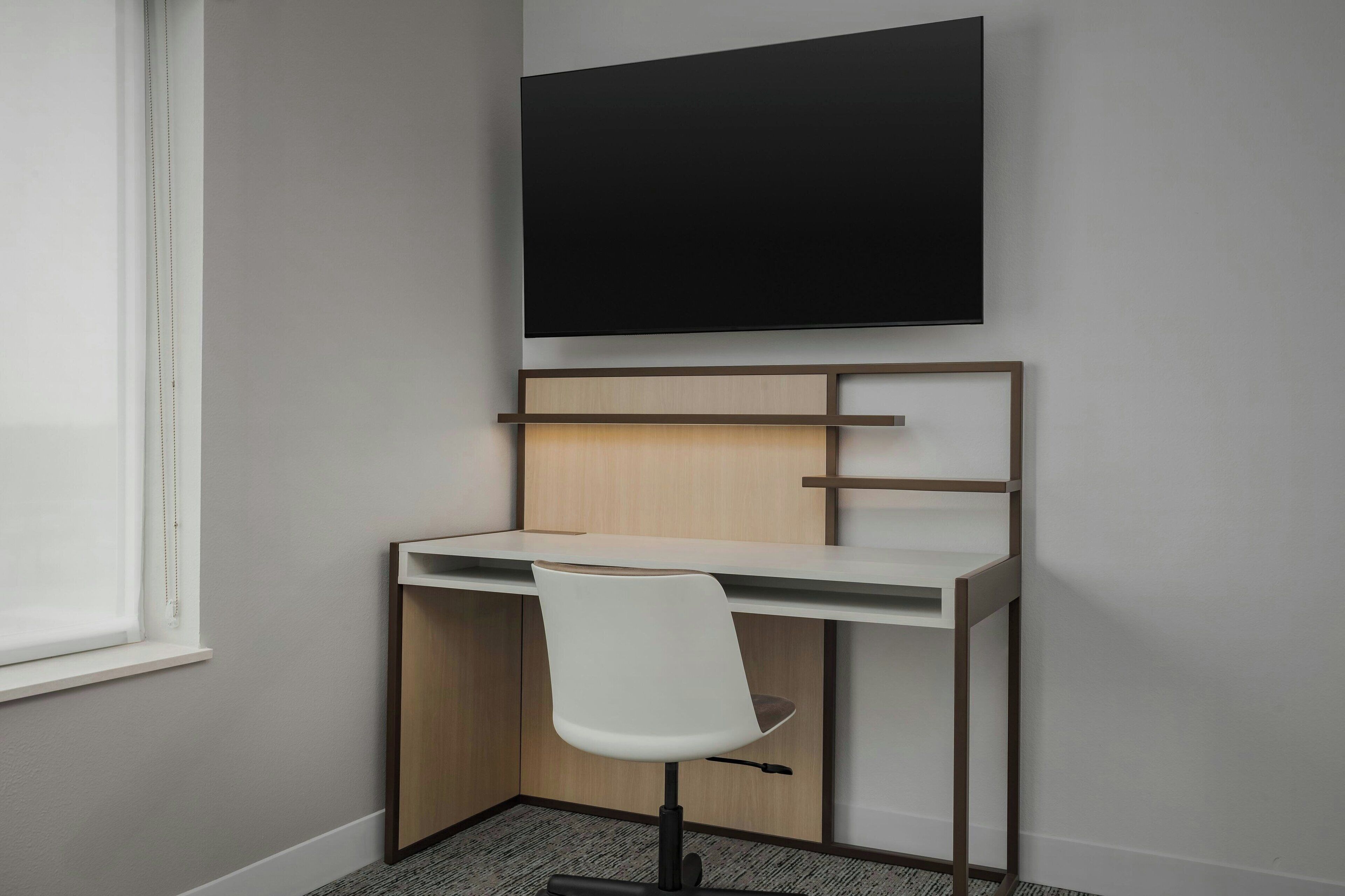 A modern office space with a desk, chair, and a mounted flat-screen TV.