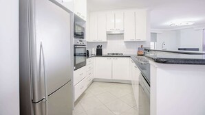 Una cocina moderna con armarios blancos, electrodomésticos de acero inoxidable y suelo de baldosas.