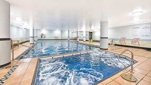 Una gran piscina interior con agua cristalina, suelo de baldosas y algunas tumbonas.