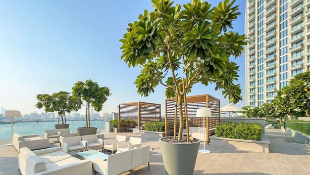 Un espace de détente aménagé sur le toit, avec des sièges extérieurs, un grand bac à plantes contenant des arbres et une vue sur le panorama urbain.