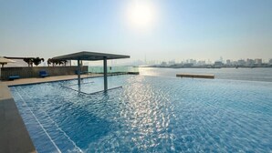 Une piscine à débordement offrant une vue sur les toits de la ville, un espace salon abrité et un ciel dégagé.