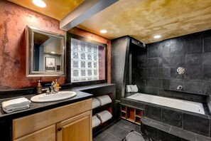 A modern bathroom with a large mirror, a sink, a bathtub, and a vanity with towels.