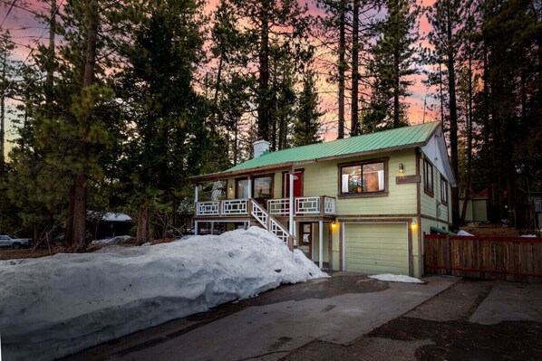 A two-story cabin with a green roof, a front porch, and a garage.