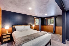 A modern bedroom with a large bed, two bedside lamps, a nightstand, and a window with curtains.
