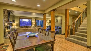 A spacious living room with a large dining table, comfortable seating, and a staircase leading to an upper level.