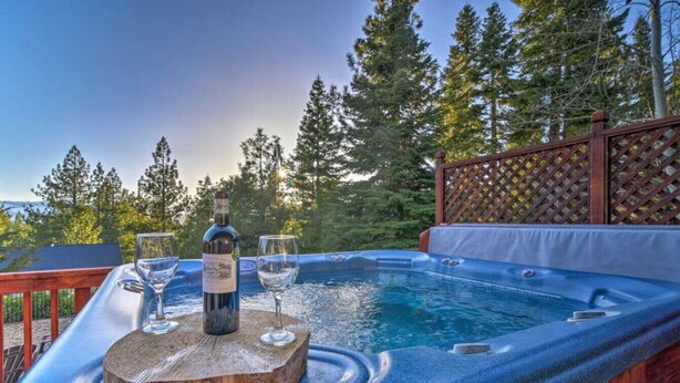 A hot tub with a wooden deck, surrounded by a wooden fence and trees.