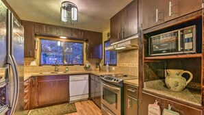 A kitchen with wooden cabinets, stainless steel appliances, a window, and a microwave on the countertop.