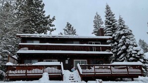 A two-story lodge with a wooden exterior, a balcony on the upper floor, and a snow-covered entrance.