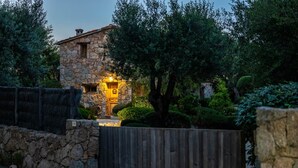 Un edificio in pietra con una porta di legno e interni illuminati, circondato da alberi e una recinzione in legno.