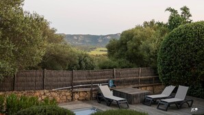 Una terrazza esterna con poltrone relax, un tavolo in legno e un muro in pietra.