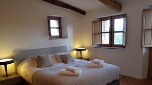 Una camera da letto con un letto grande, due comodini, due lampade a parete e due finestre con persiane aperte.