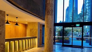 A hotel lobby with a reception desk, large pillars, and a view of the city through glass doors.