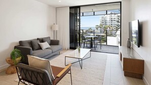 A modern living room with a grey sofa, a coffee table, and a view of a balcony with outdoor furniture.