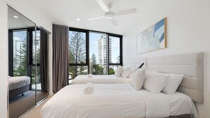 A modern hotel room with a large bed, a ceiling fan, and a city view through large windows.