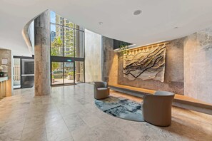 Un lobby espacioso con diseño moderno, que incluye una gran obra de arte en la pared, zonas de estar y una entrada de cristal.