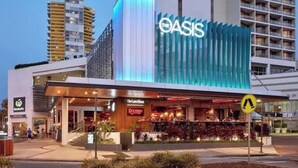 Ein modernes Hotel mit einem gut sichtbaren 'OASIS'-Schild, einem Restaurant namens 'The Coconut Bar' und einem Fußgängerüberweg-Schild.