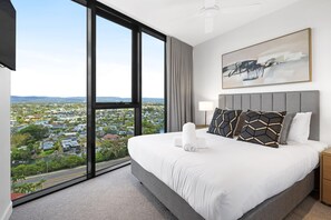 Ein Hotelzimmer mit einem großen Bett, Blick auf eine Stadtlandschaft, einem Gemälde an der Wand und einer Lampe auf dem Nachttisch.