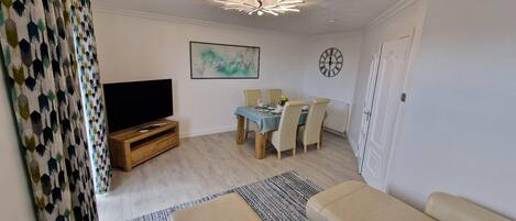 A living room with a TV, dining table, chairs, and a sofa.